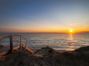 Eine Holztreppe führt zu einem Strand, während die Sonne über dem Meer untergeht.