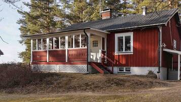 A red wooden house with a porch, a chimney, and a small attached structure.