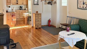 Ein gemütliches Wohnzimmer mit Holzboden, einem grünen Sofa, einem kleinen Tisch mit Fernbedienung und einer Küche im Hintergrund.