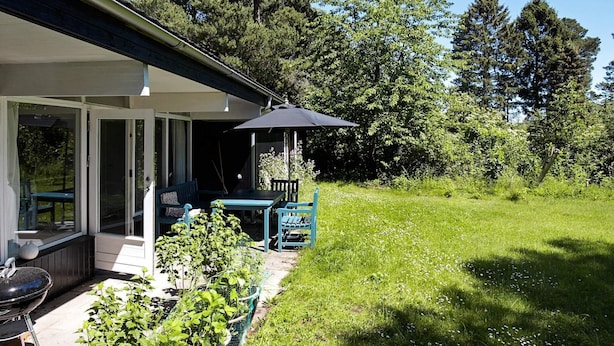 A covered patio with a table and chairs, a grill, and a garden area with plants and a fence. - 4 Person Holiday Home in Hornbaek (Hornbaek)