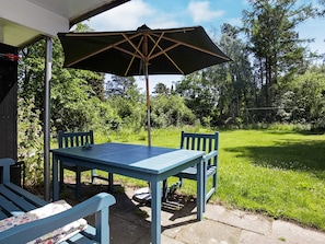 An outdoor patio with a table and chairs, a large umbrella, and a view of a grassy area with trees. - 4 Person Holiday Home in Hornbaek (Hornbaek)