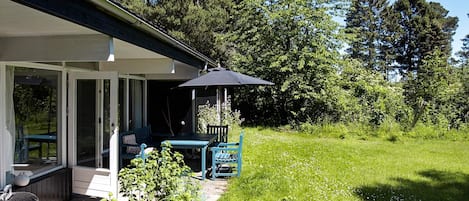 A covered outdoor seating area with a table and chairs, a grill, and a garden with a fence.