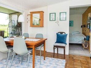 Uma área de refeições com mesa e cadeiras de madeira, um banco e vista para um jardim através de uma porta de vidro.