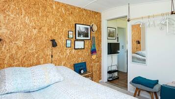 Ein Schlafzimmer mit Bett, Fernseher, Spiegel und einer Tür zu einem anderen Raum.