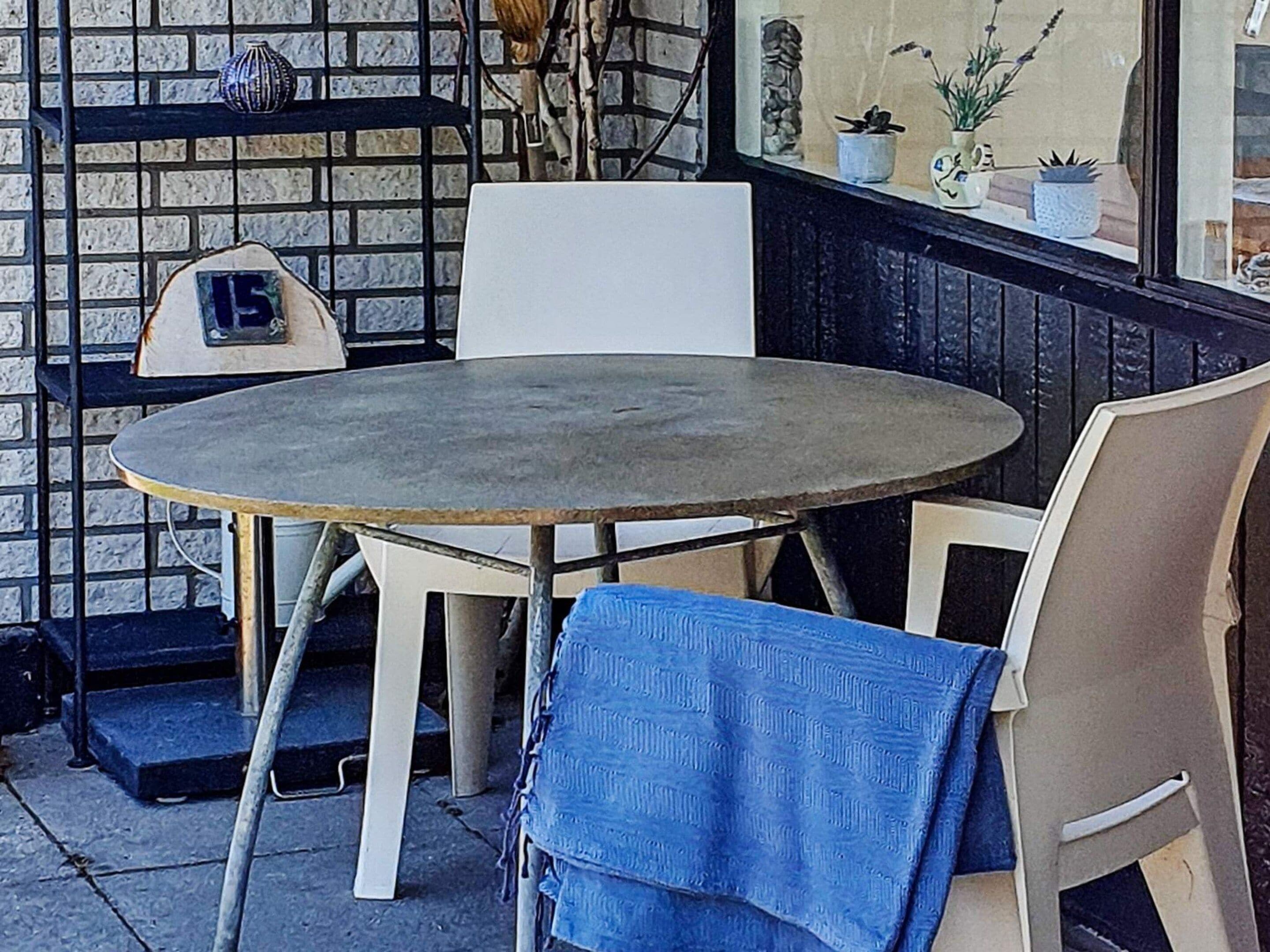 Ein runder Tisch mit Stühlen, ein weißer Stuhl und ein blaues Tuch, das über einem Stuhl drapiert ist.