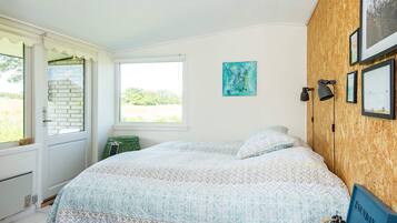 Ein Schlafzimmer mit einem Bett, einem Fenster, einem Wandbild und einem kleinen Tisch mit einer Lampe.