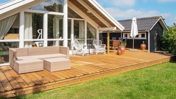 A modern house with a large deck, white wicker furniture, and a black shed in the background. - 6 Person Holiday Home in Hemmet (Hemmet)