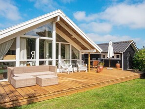 A modern house with a large deck, white wicker furniture, and a black shed in the background.