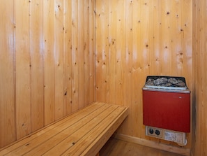 A wooden sauna room with a bench and a sauna unit.