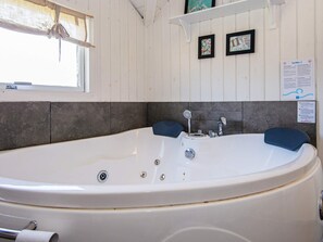 A bathroom with a large bathtub, a shower, and a window. There are two framed pictures on the wall and a sign with information.