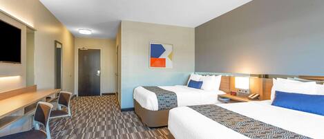A hotel room with a large bed, a desk with a chair, a TV, and a door leading to another room.
