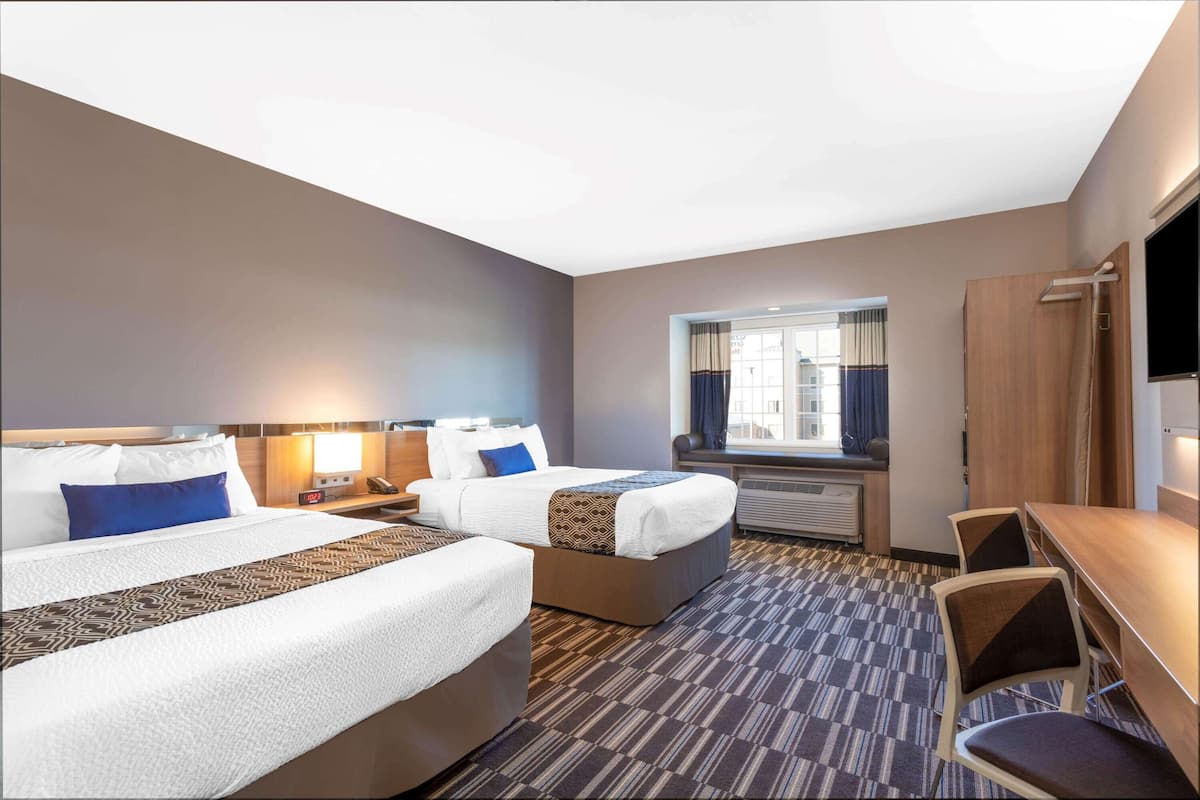 Habitación de hotel con dos camas, un escritorio, una silla, un televisor y una ventana con cortinas.