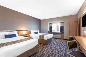 Habitación de hotel con dos camas, un escritorio, una silla, un televisor y una ventana con cortinas.