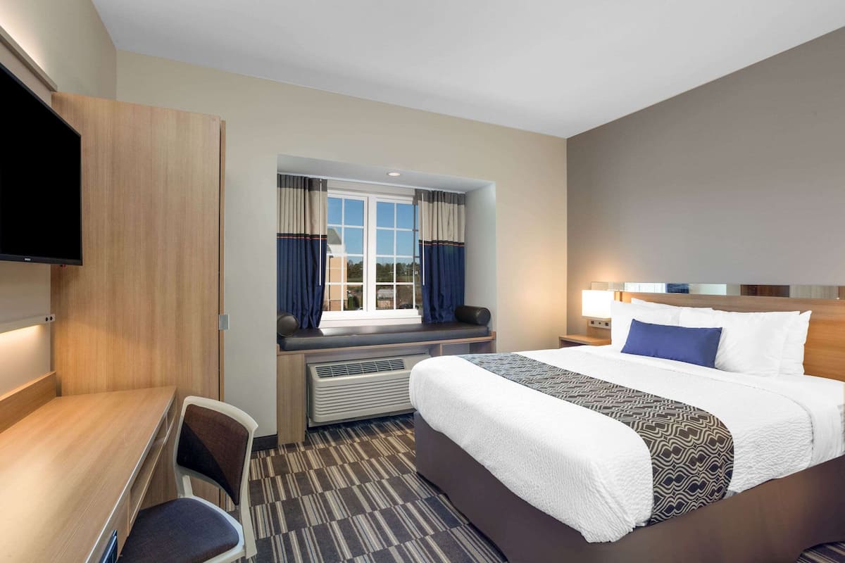 Una habitación de hotel con una cama grande, un escritorio, una silla, un televisor y una ventana con cortinas.