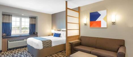 Habitación de hotel con cama, sofá, una mesita y ventana con cortinas.