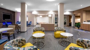 Een moderne hotel lobby met hexagonaal patroon zitplaatsen, een flatscreen televisie en een receptiebalie.