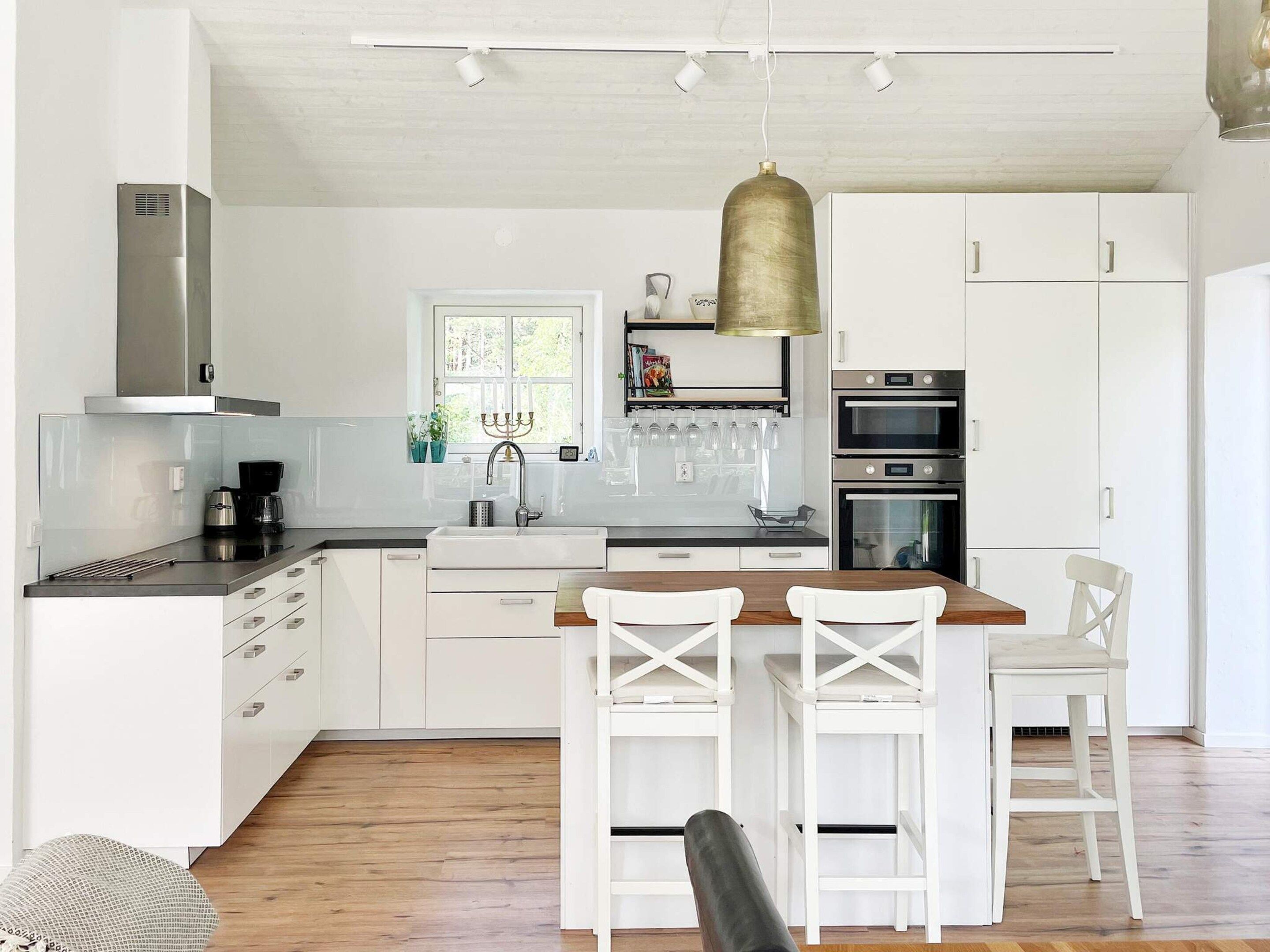 Une cuisine moderne avec des meubles blancs, un îlot central en bois doté de tabourets, et des appareils électroménagers intégrés.