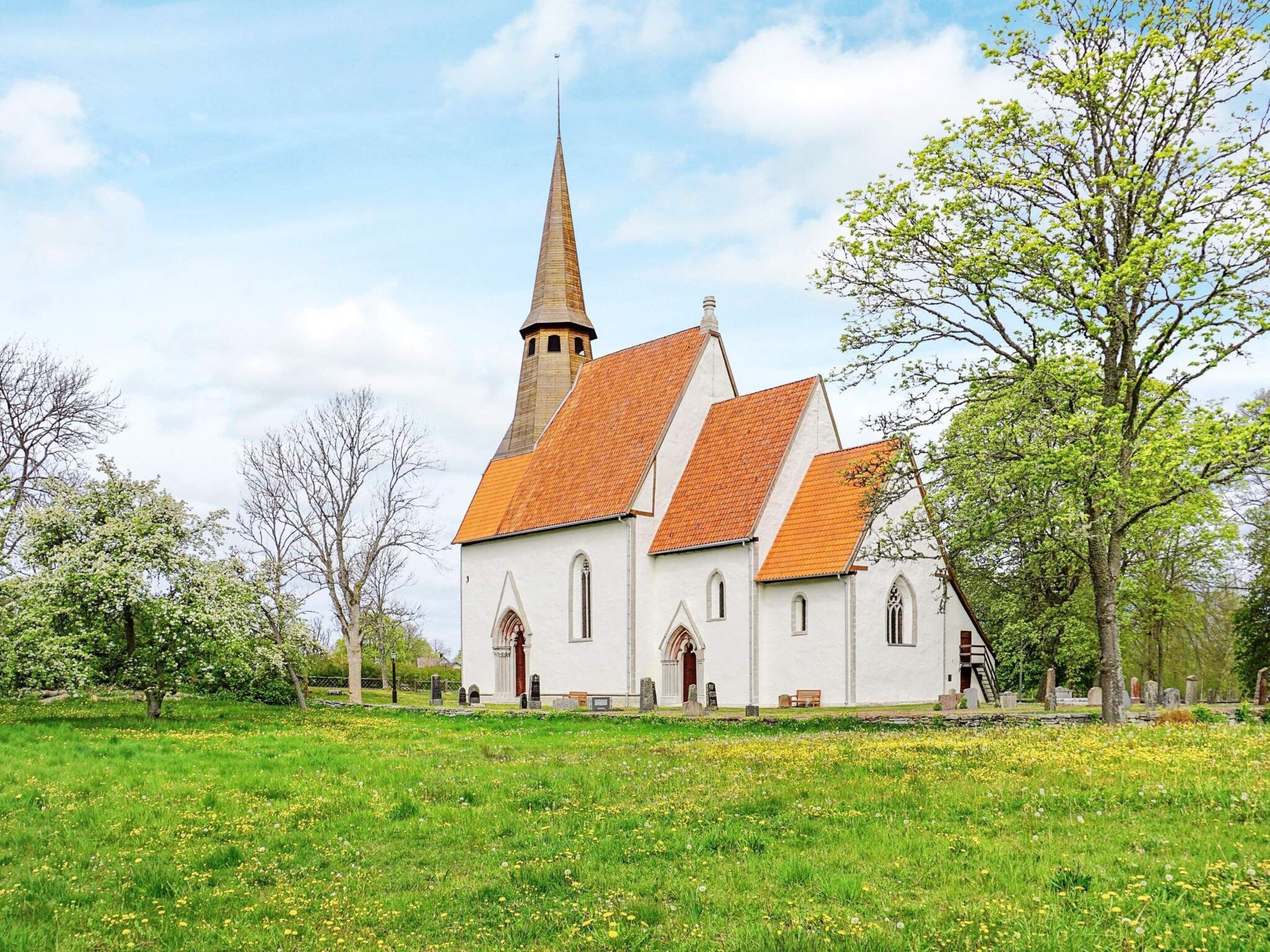 A church with a tall spire and a traditional design, surrounded by a grassy field and trees.