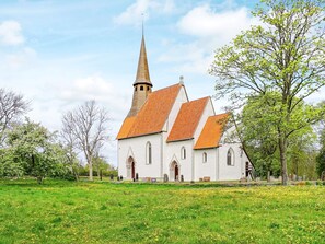 Une église dotée d’un clocher imposant et d’une architecture traditionnelle, entourée d’un champ verdoyant et d’arbres.