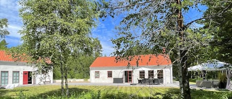 A building with a red roof, surrounded by greenery, and a clear sky.