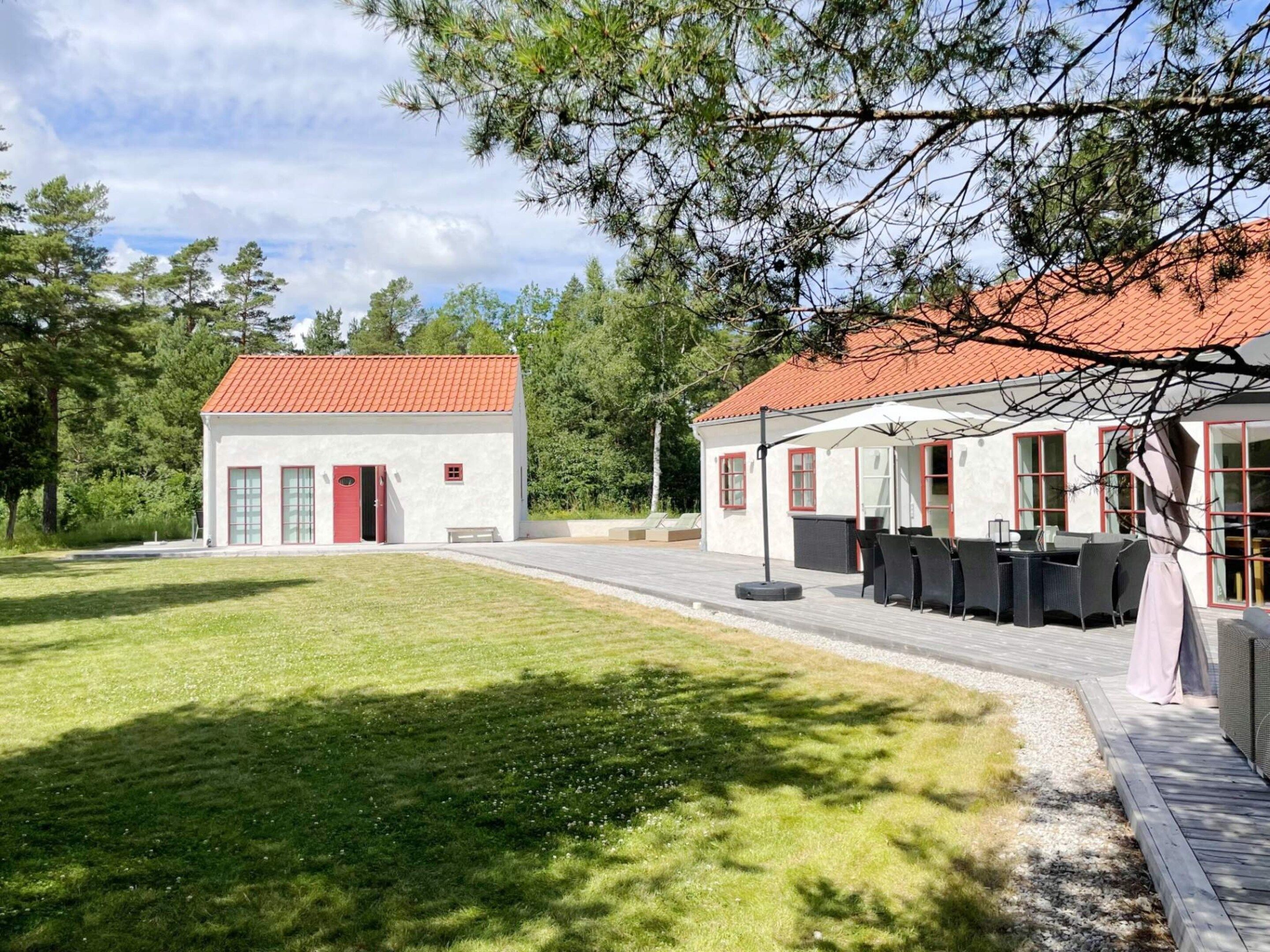 A two-story building with a red-tiled roof, a covered outdoor seating area with tables and chairs, and a well-maintained lawn.