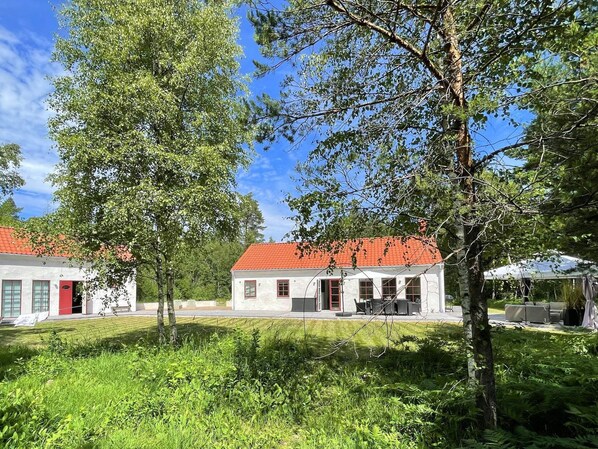 A two-story building with a red-tiled roof, surrounded by lush greenery and trees. - Holiday Home in Katthammarsvik (Katthammarsvik)