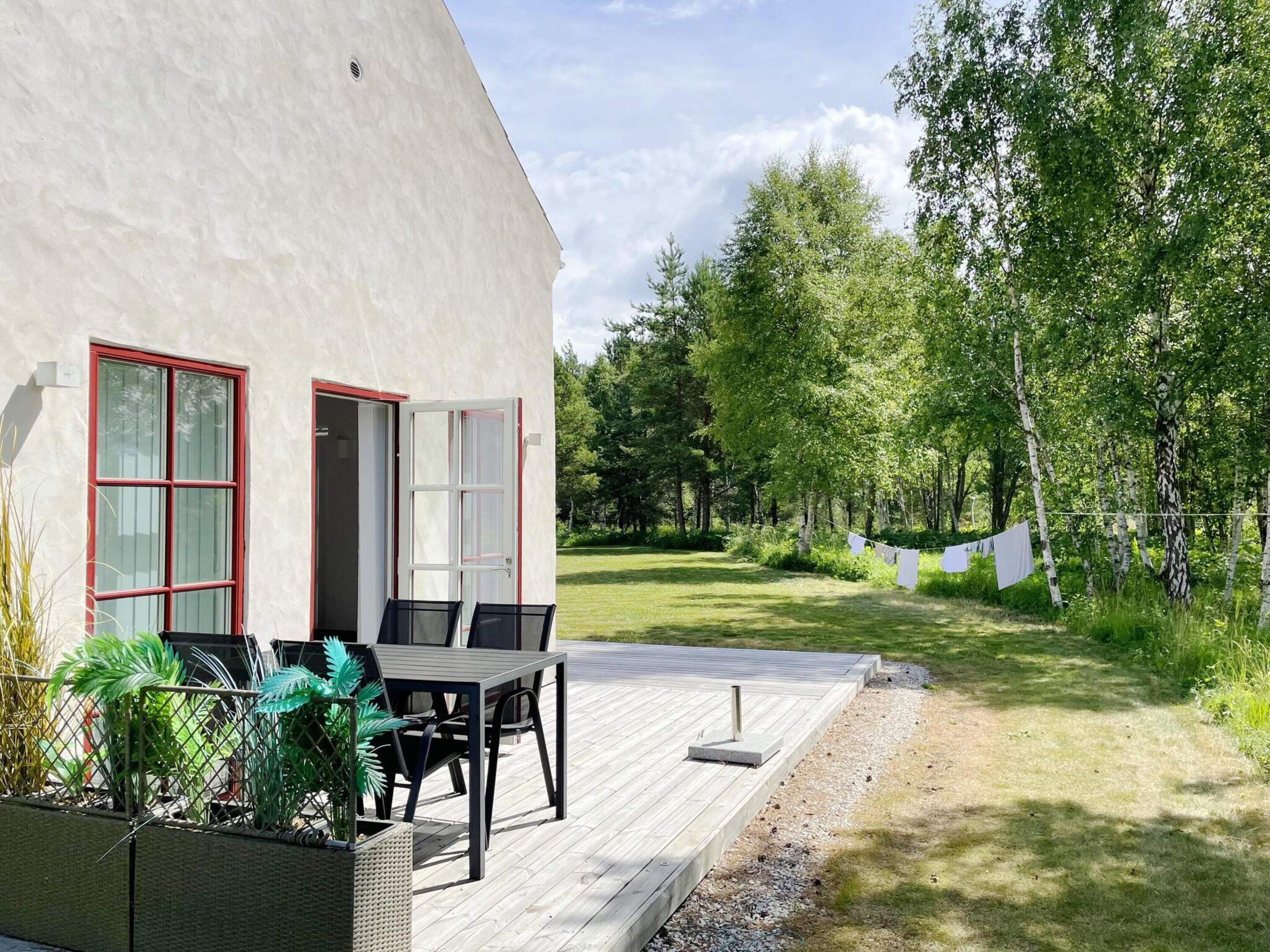 A modern house with a deck, a dining area, and a garden with trees and a clothesline.