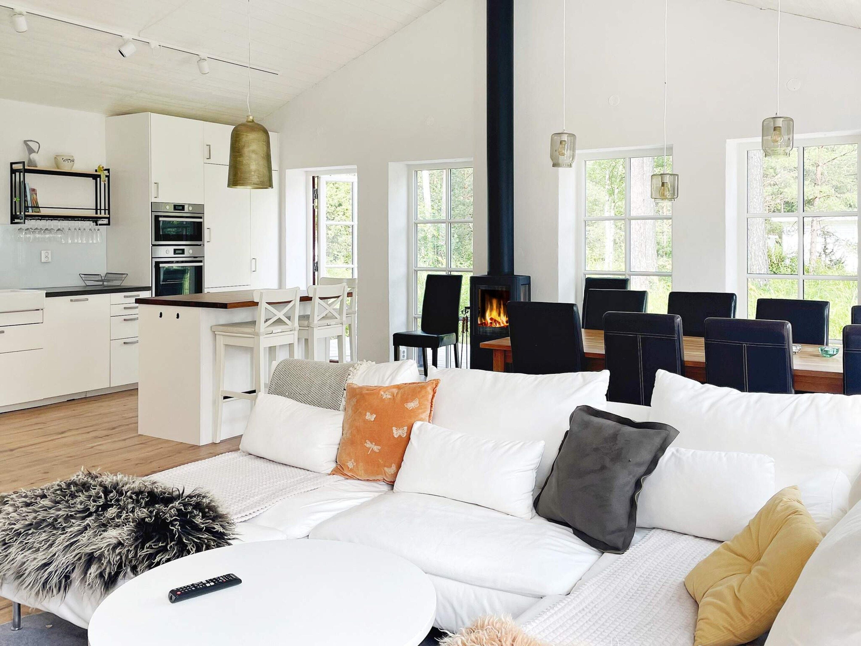 A modern living room with a sofa, a dining area with chairs, a kitchen with appliances, and a fireplace.