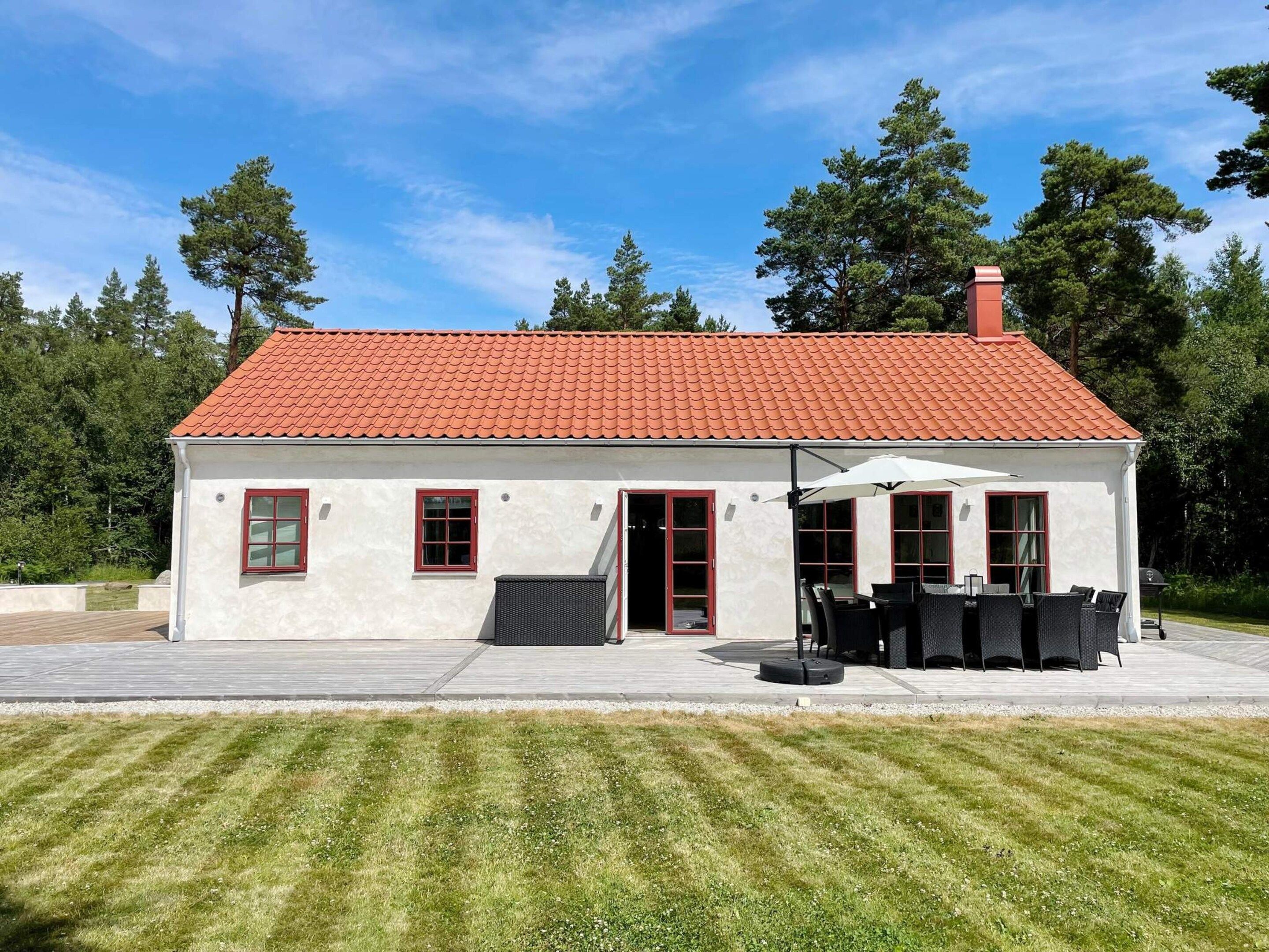 Un bâtiment d’un seul étage, doté d’un toit recouvert de tuiles rouges, d’un patio abrité avec des meubles d’extérieur et d’une pelouse bien entretenue.