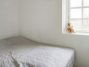 A single bed with a quilted cover in a room with white walls and a window.