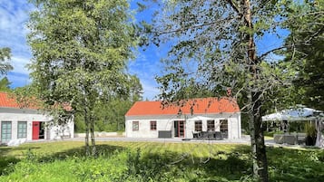 A two-story building with a red-tiled roof, surrounded by lush greenery and trees.