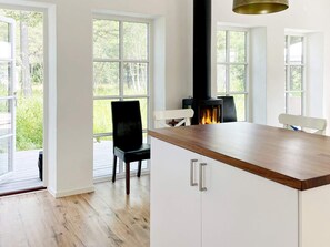 A modern kitchen with a central island, white cabinetry, and a wood-burning stove. - Holiday Home in Katthammarsvik (Katthammarsvik)