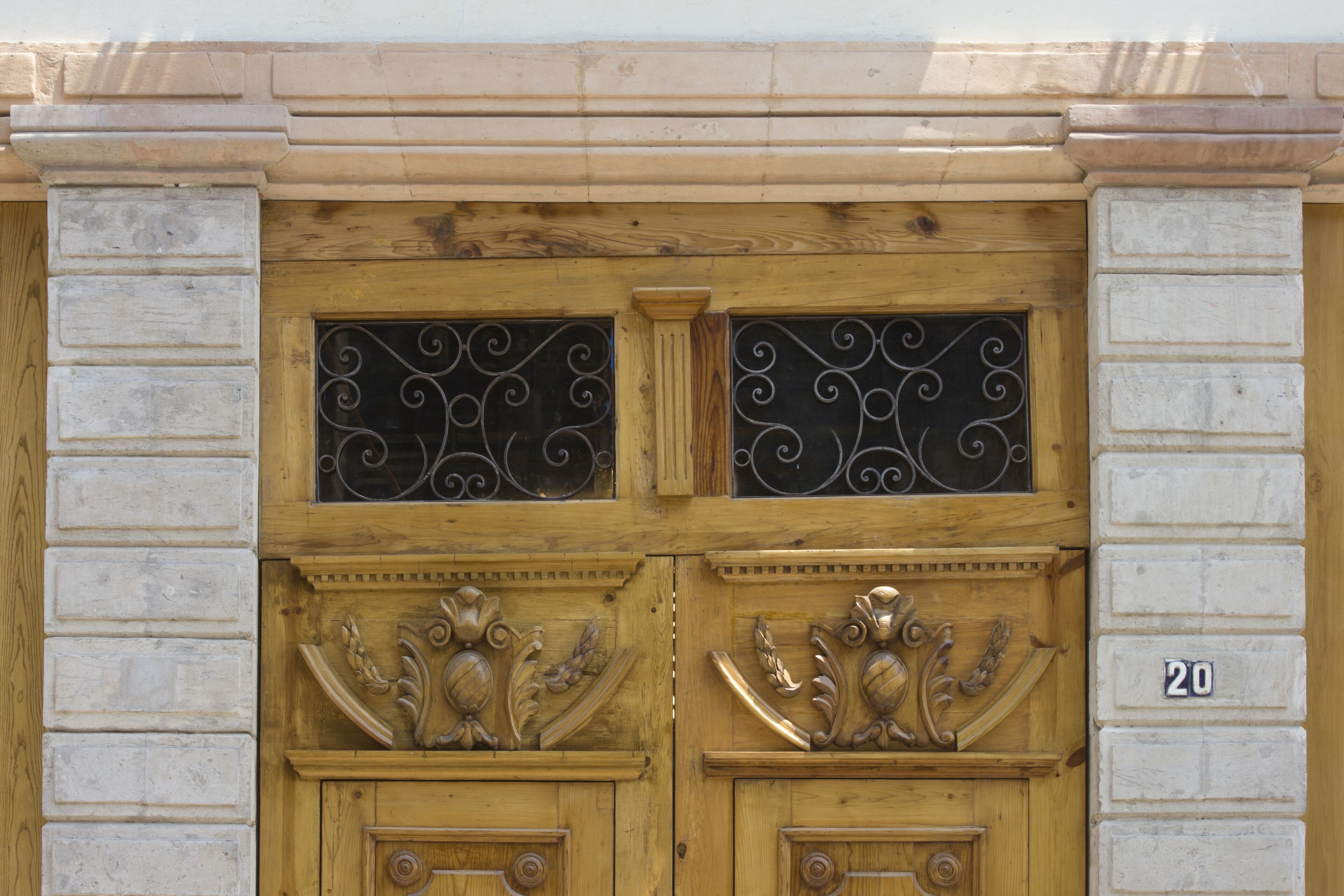 Una puerta doble de madera con adornos decorativos y el número 20 en el lado derecho.