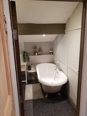 A bathroom with a freestanding bathtub, a small table with a plant, and a mirror on the wall. - Albert Rd (Colne)
