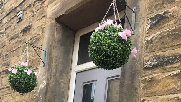 A stone building with a grey door and a hanging flower basket. A sign indicates "Albert Rd Apartment." - Albert Rd (Colne)