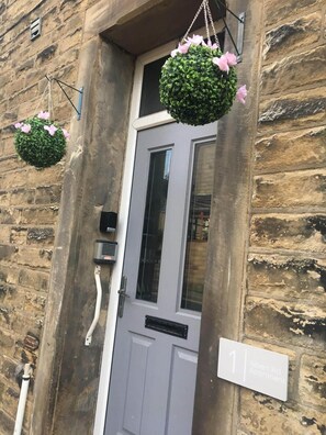 A stone building with a grey door and a hanging flower basket. A sign indicates "Albert Rd Apartment." - Albert Rd (Colne)