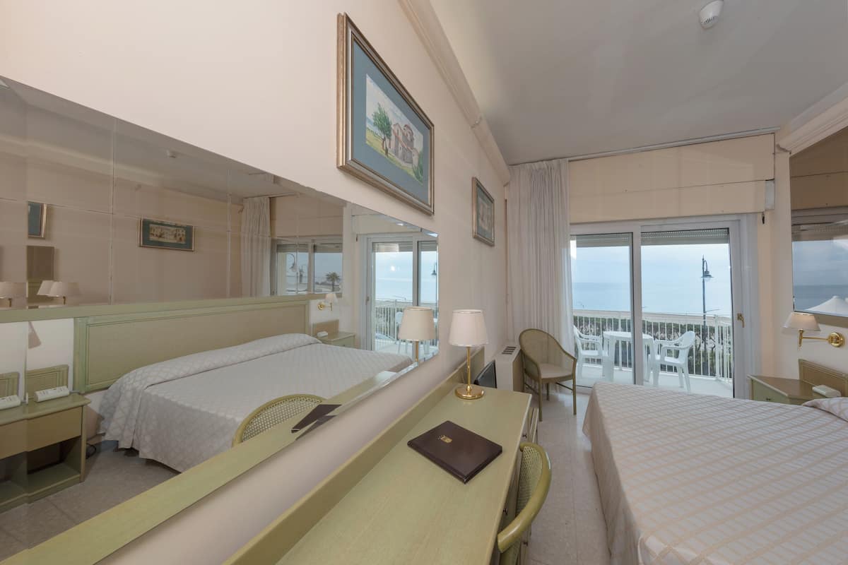 A hotel room with two beds, a desk, a chair, a balcony with a view, and a large mirror.