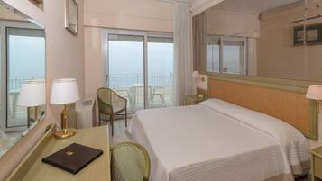 Ein Hotelzimmer mit einem großen Bett, einem Schreibtisch mit Stuhl, einem kleinen Tisch und einem Fenster mit Meerblick.