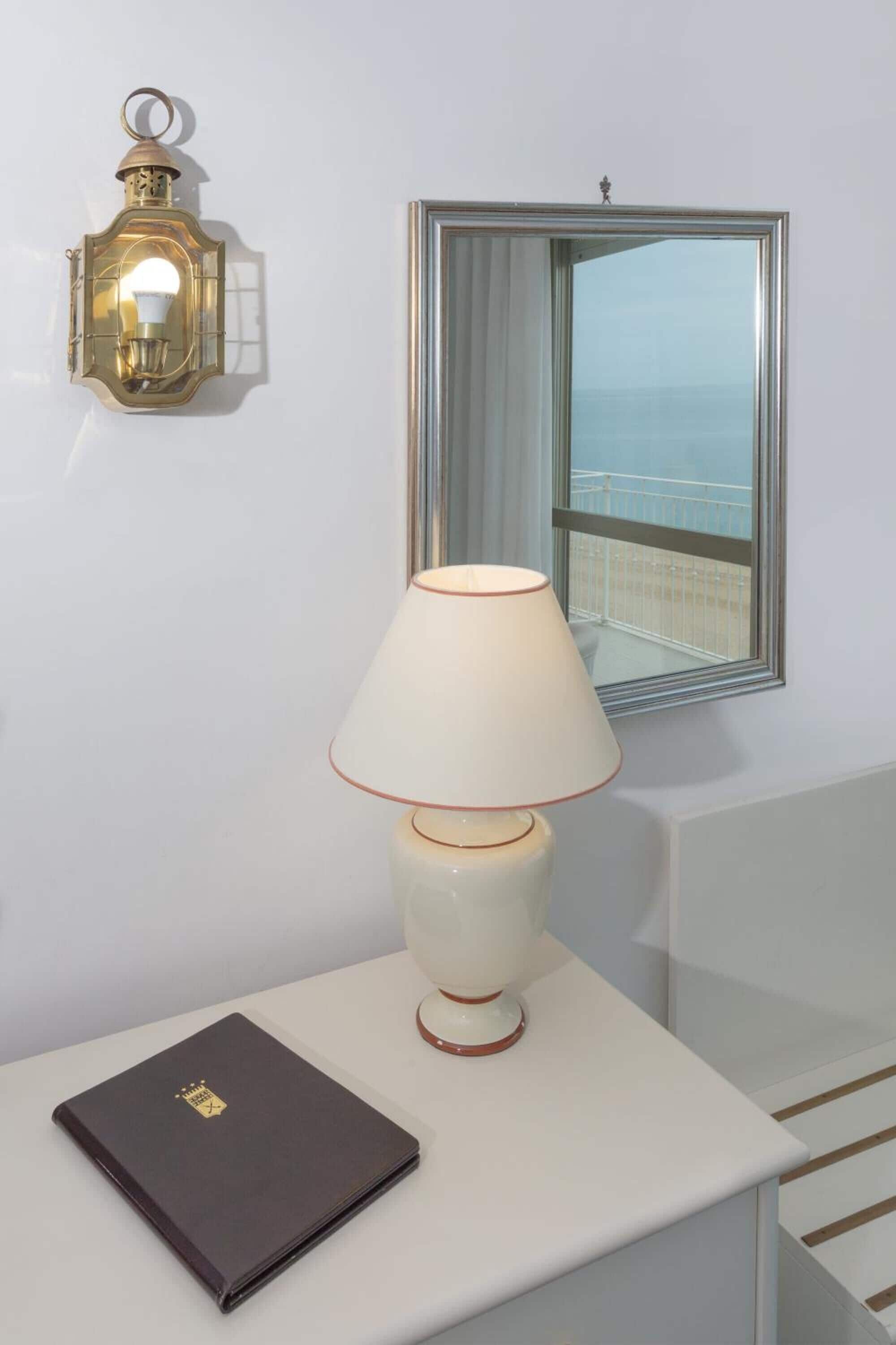 Ein Zimmer mit einem weißen Tisch, einer Lampe, einem Wandleuchter und einem Fenster mit Blick.