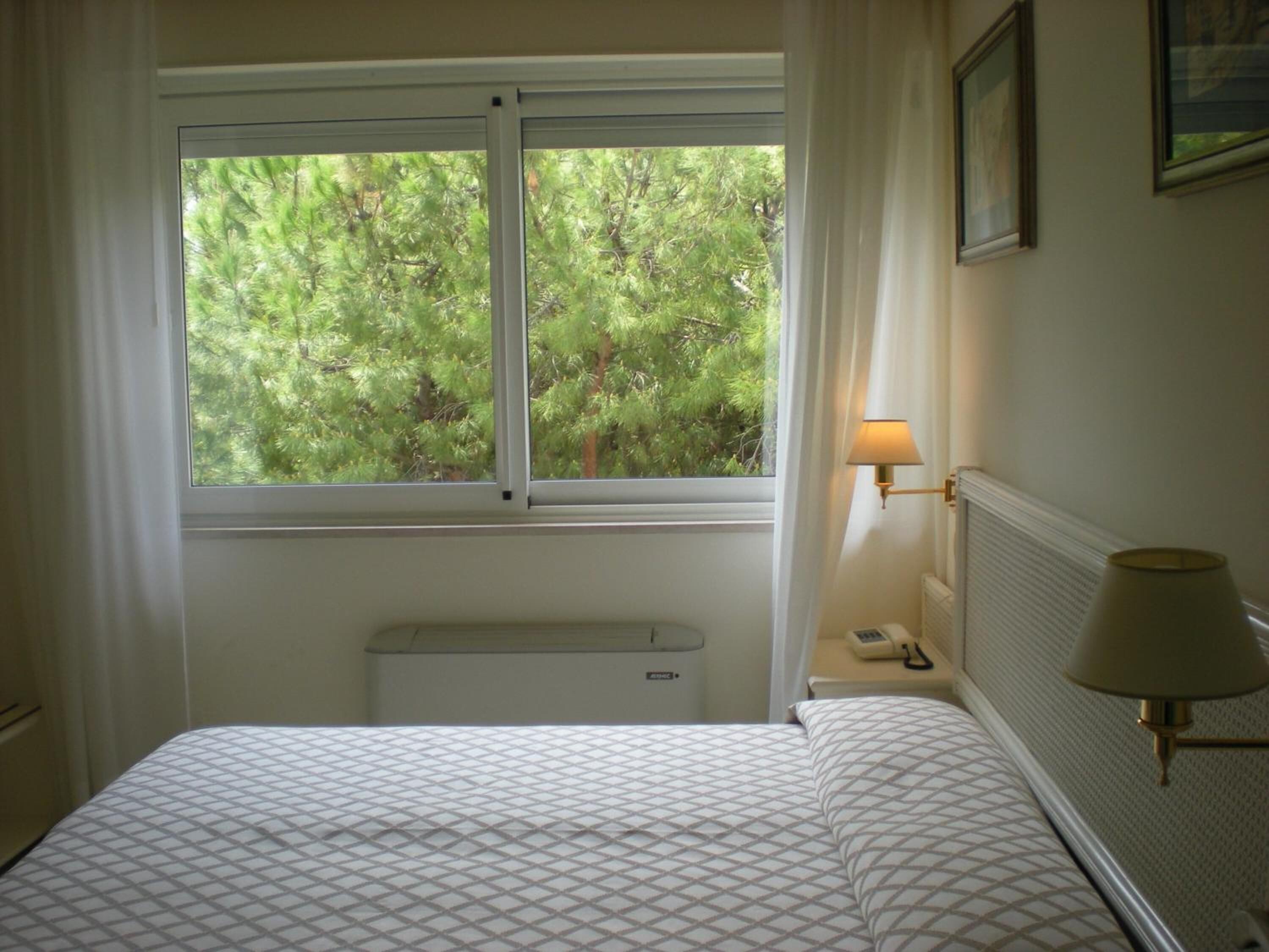 A bedroom with a bed, a window with curtains, a radiator, and a wall-mounted lamp.