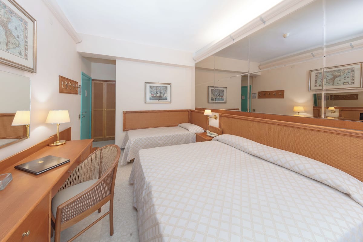 A hotel room with two beds, a desk, a chair, a mirror, and a door leading to a bathroom.