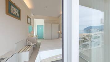 Quarto de hotel com cama, cadeira, escrivaninha e vista para a paisagem urbana através de uma varanda.