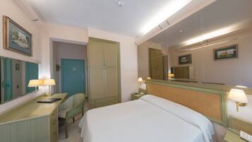 Quarto de hotel com cama, escrivaninha com luminária, cadeira, armário e espelho.