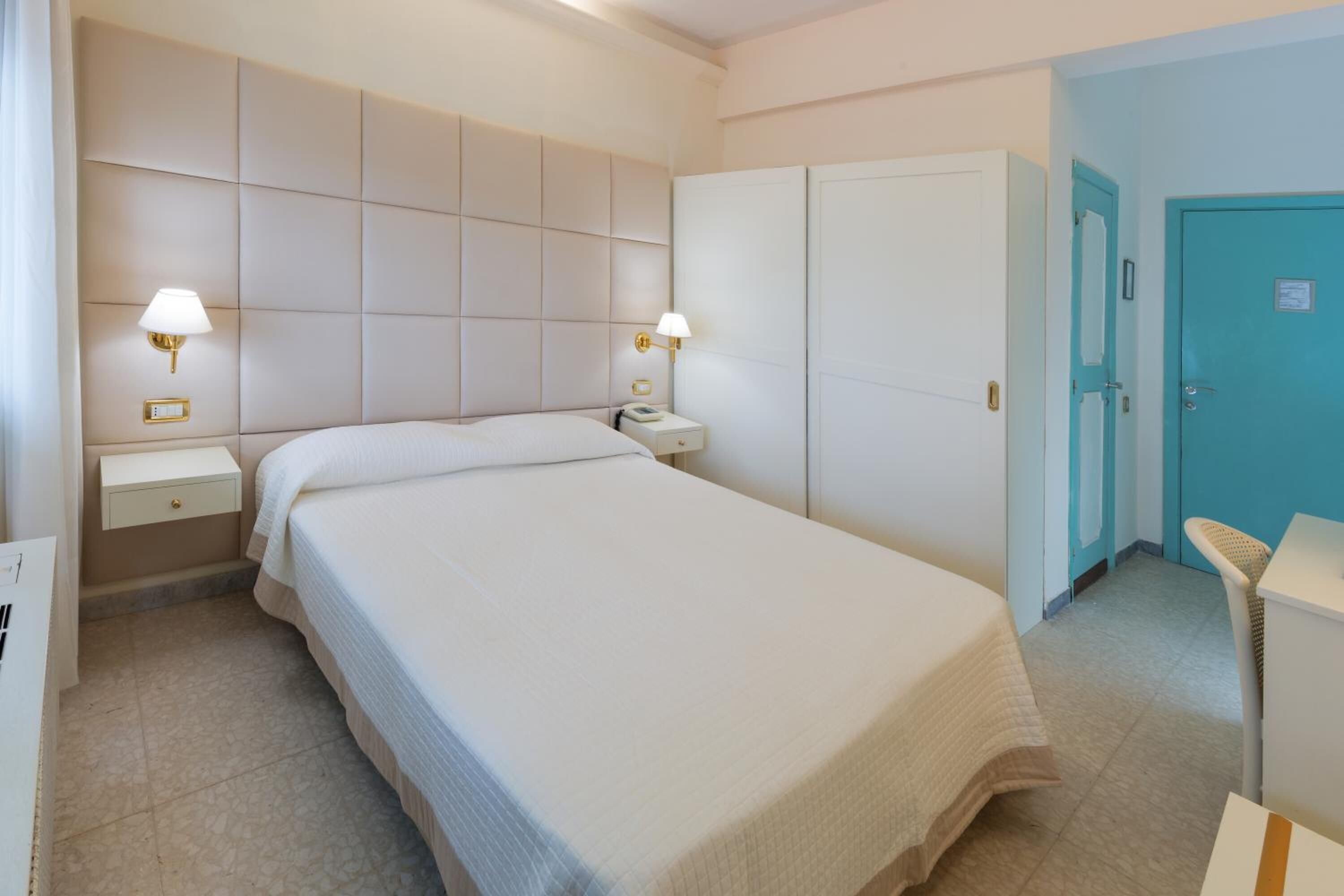 A hotel room with a large bed, bedside tables, a wardrobe, and a bathroom door.