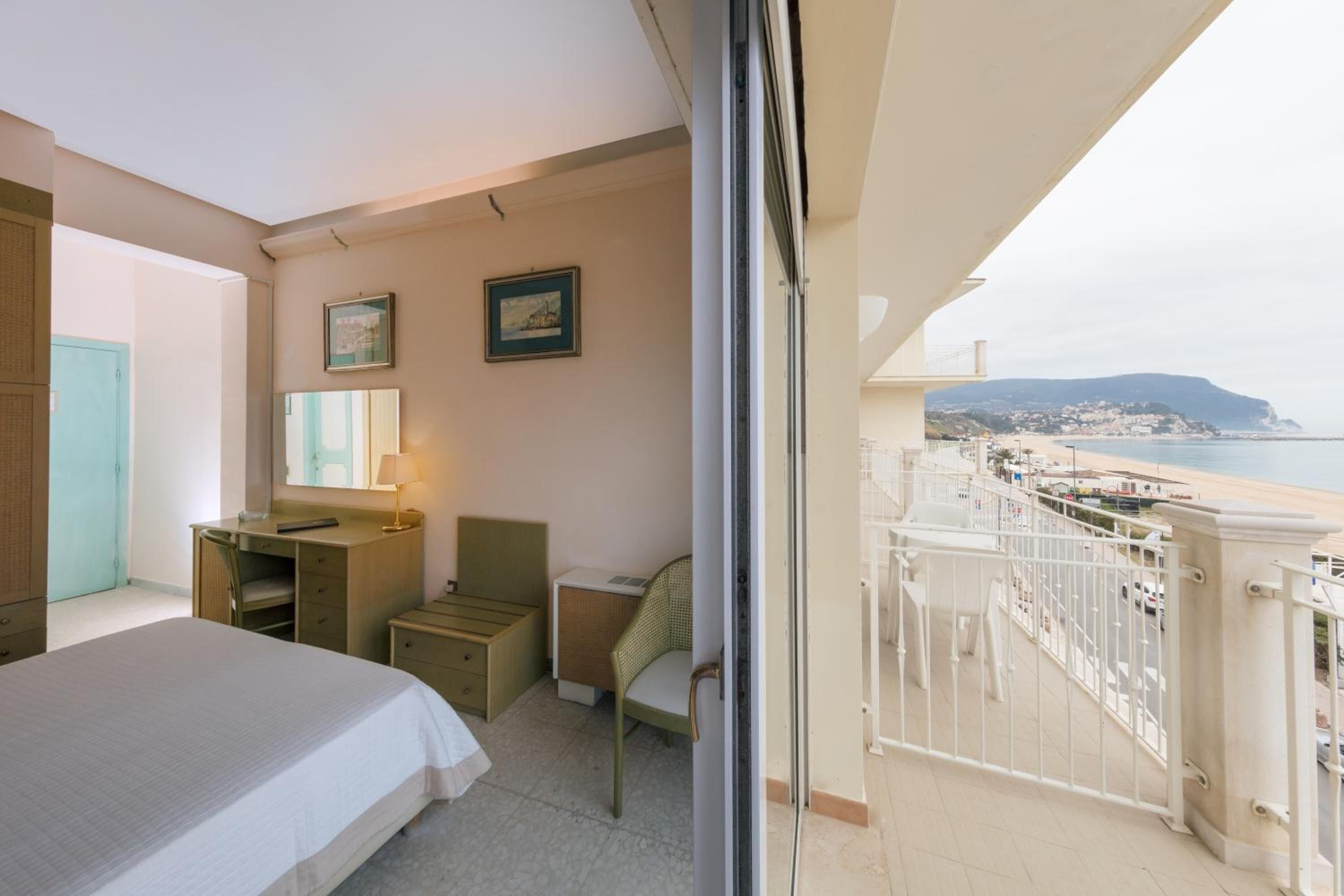 Camera d'albergo con un letto, una scrivania, una sedia e un balcone vista spiaggia e città.