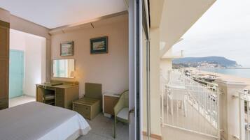 Camera d'albergo con un letto, una scrivania, una sedia e un balcone vista spiaggia e città.
