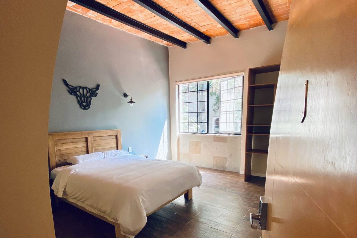 A bedroom with a bed, wooden floor, a bull head decoration, a window, and a door.