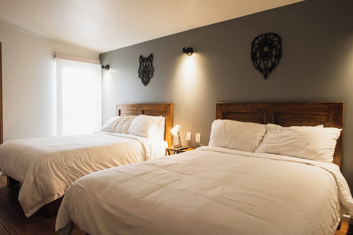 A hotel room with two beds, a nightstand with a lamp, and decorative wall art.