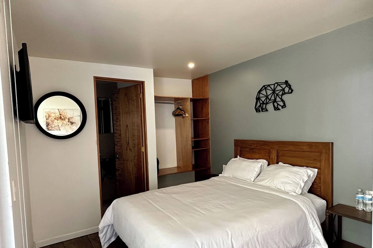A bedroom with a large bed, a wooden headboard, a wardrobe, and a wall-mounted artwork of a geometric pattern.