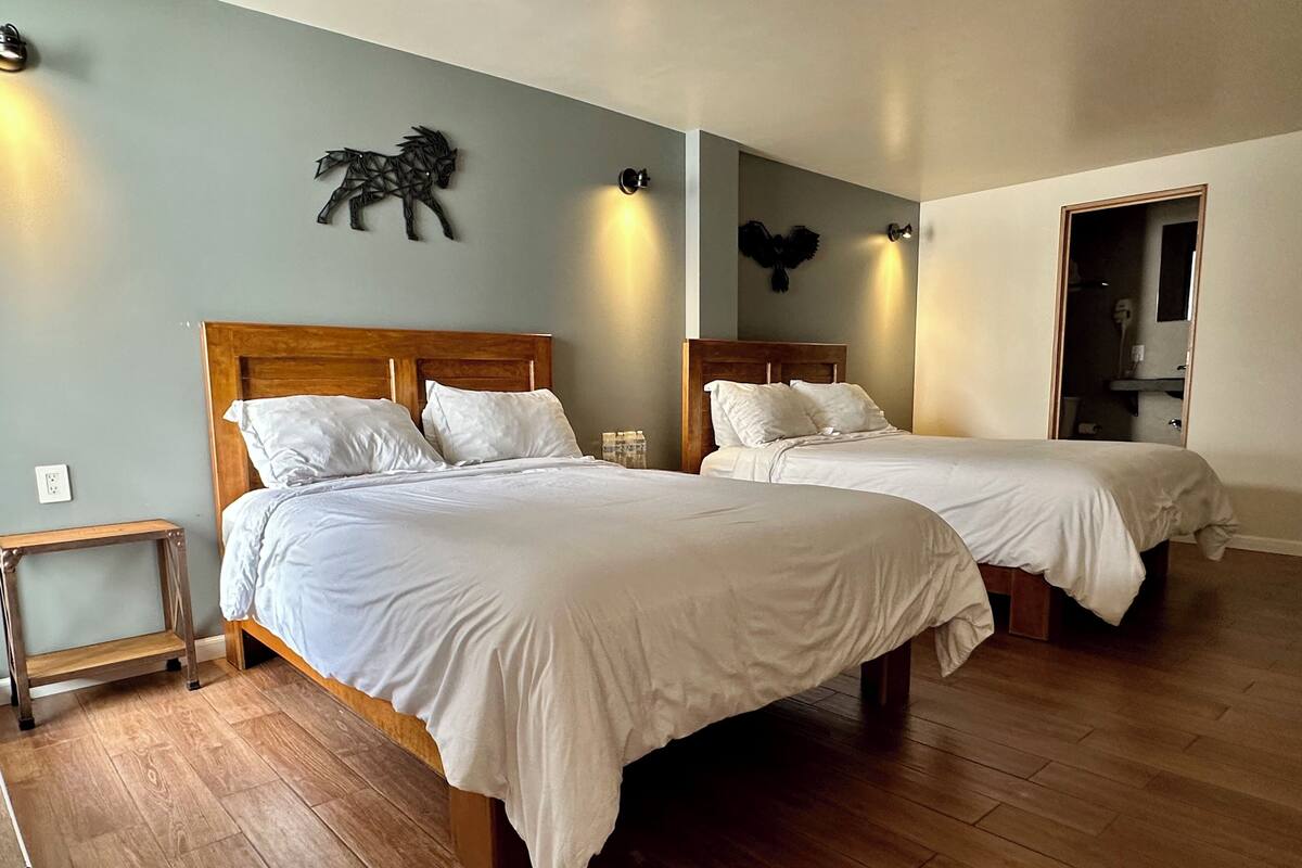 A hotel room with two beds, wooden flooring, and decorative wall art.